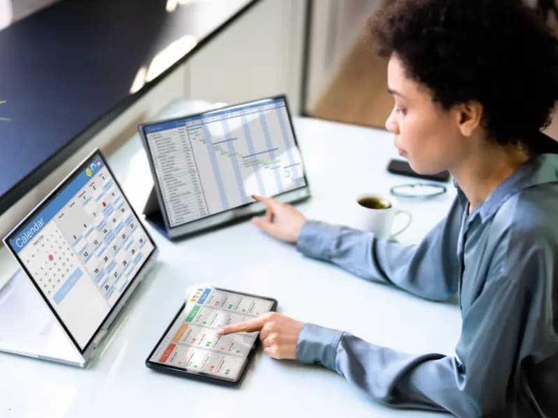 Online scheduling software displayed on multiple screens as a woman manages tasks and calendars at her desk