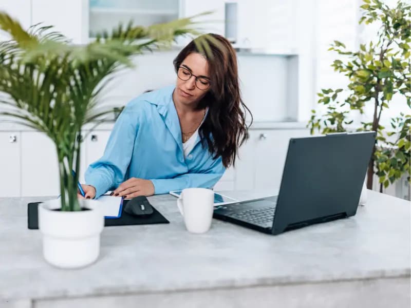 Scheduling software for businesses used by a woman taking notes while working remotely on her laptop.